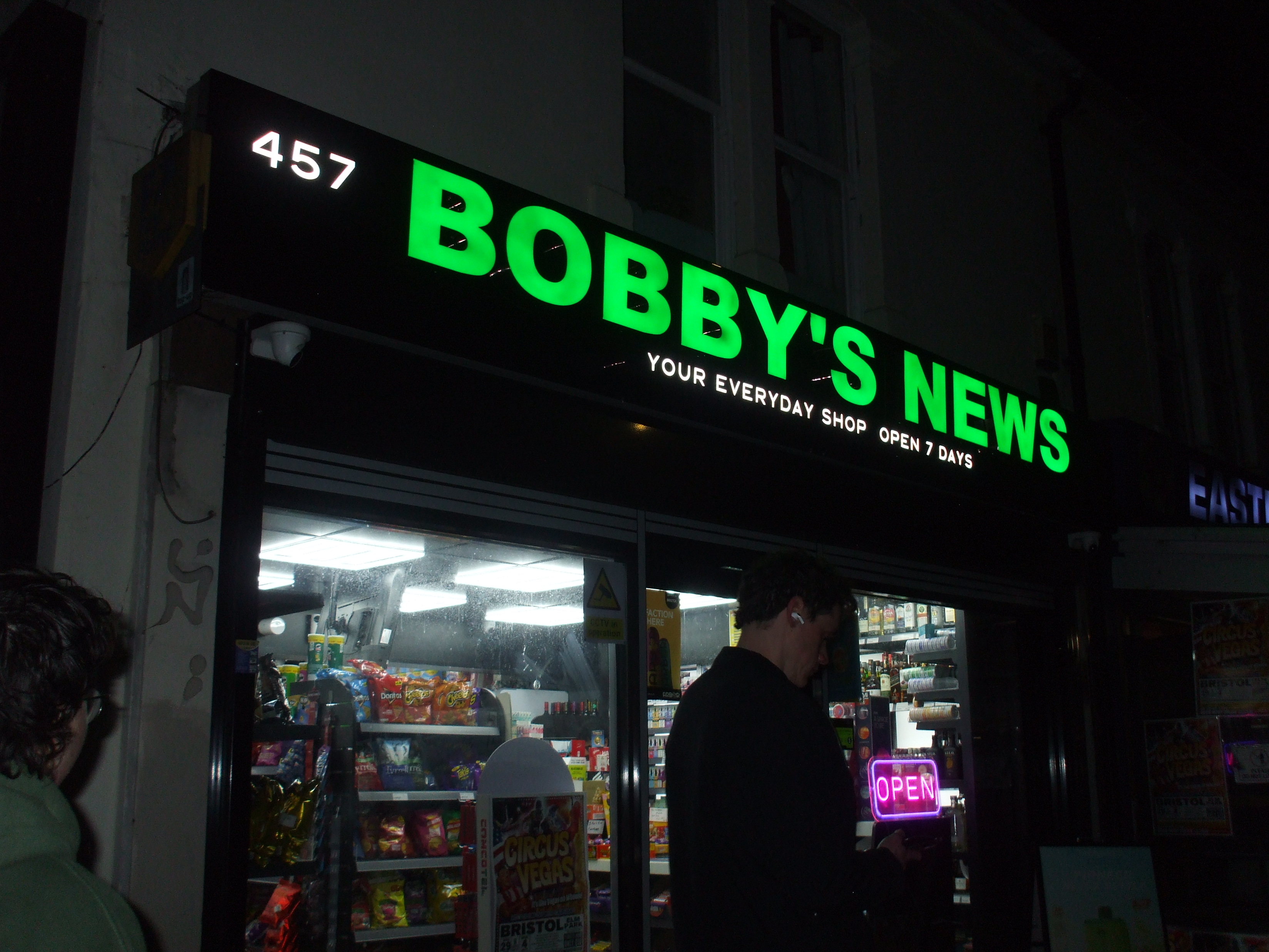 Bobby's News late at night. The green sign is glaringly bright.